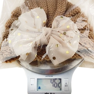 Detailed weight measurement of a brown knit baby hat with a gold polka dot mesh bow