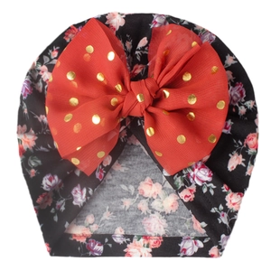 Detail of baby turban hat featuring floral print and large red bow with gold polka dots
