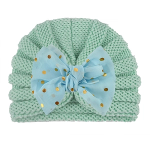 Detailed close-up of mint green knitted baby turban hat with a blue polka dot bow