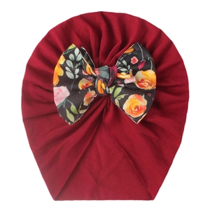 Detail of baby turban hat in deep red with a large floral print bow decoration