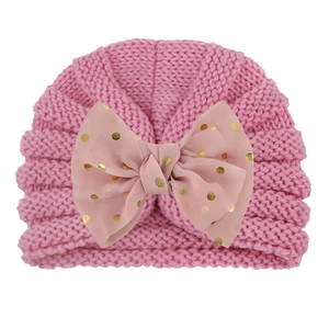 Pink knit baby hat detail showing soft wave texture and gold polka dot bow accent