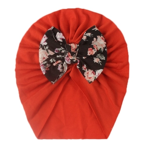 Detailed view of red infant turban hat featuring a large floral bow on soft knit fabric