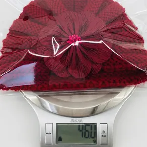 Detail view of red knitted baby flower hat on a scale showing a lightweight 46g weight