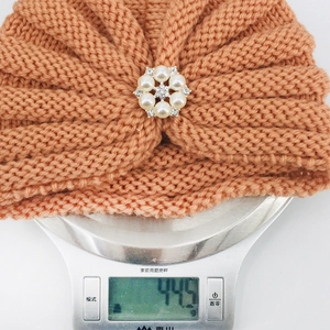 Détail du bonnet turban en tricot rose pêche avec broche décorative en perles et cristaux