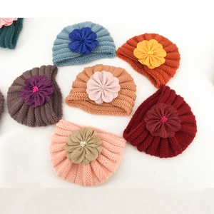 Knitted baby turban hats with large fabric flowers in assorted colors on white background