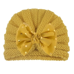 Close-up of baby winter knit hat with large yellow tulle bow and gold foil polka dots