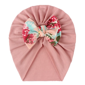Close-up of baby hat featuring a large floral print bow on soft pink knit fabric