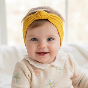 Detail of baby yellow knotted ribbed cotton headband worn by infant in soft knit sweater