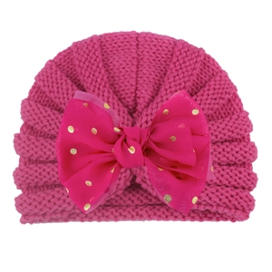 Close-up of pink baby knitted hat featuring a large gold polka dot tulle bow accent
