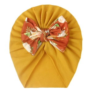 Detail of baby mustard yellow turban hat with large orange floral print bow decoration