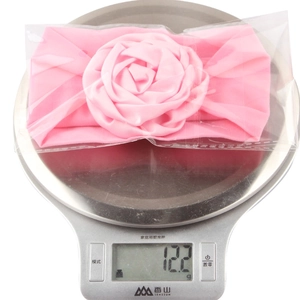Pink nylon baby headband with 3D ribbon rose detail being weighed on scale at 12.2g