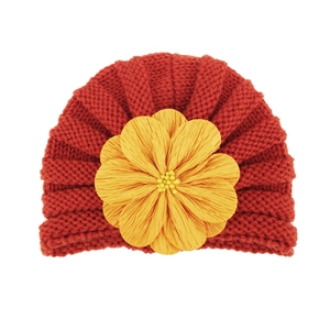 Detail of baby knit hat in brick red with large yellow flower and pearl accents