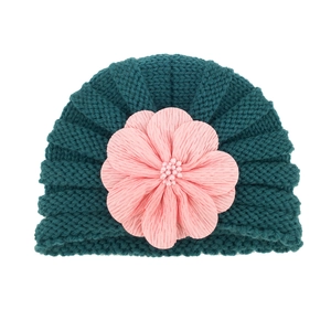 Detailed close-up of dark green knitted baby hat with large pink fabric flower detail
