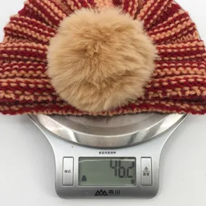 Dettaglio del cappello in maglia a righe per neonati con pompon su bilancia digitale