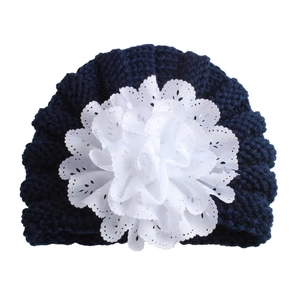 Knitted dark blue baby hat featuring a large white lace flower decoration on the front