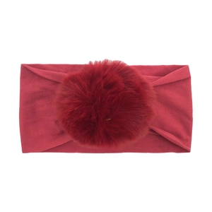 Macro detail of wine red baby nylon headband featuring a soft large plush pom-pom decoration