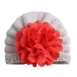 Detailed close-up of cream knit baby hat with a large red decorative lace flower