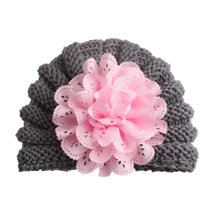 Detail of grey knitted baby hat featuring a large pink lace flower decoration