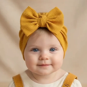 Detail of ginger yellow knitted baby hat featuring a large soft bow and ribbed texture