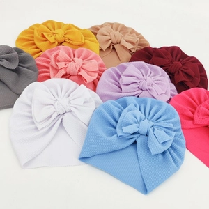 Detailed view of colorful waffle knit baby beanies with large knot bows in various soft shades