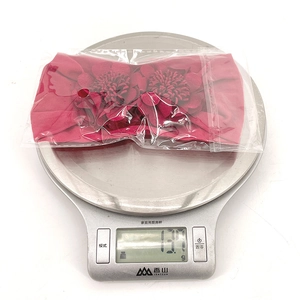 Detail showing deep pink floral baby headband in packaging weighing 13.7g on scale