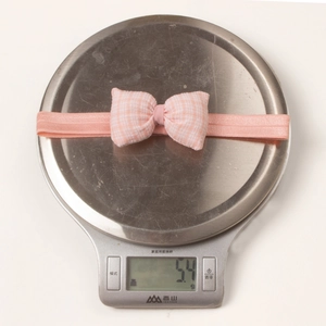 Detail shot of a pink plaid bow baby headband on a scale weighing 5.4g for infant comfort