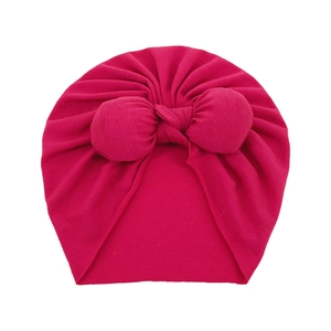 Detailed close-up of hot pink baby turban hat with a large decorative bow on white background