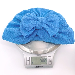 Detailed close-up of a blue knitted baby hat with a bow on a scale weighing 30 grams