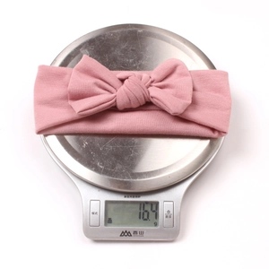 Pink soft knit baby headband with bow detail weighing 16.4g on a scale