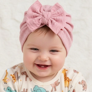 Close-up of pink knitted baby hat with large bow decoration on infant model