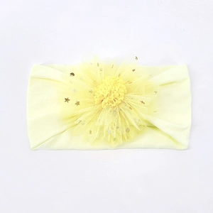 Detail eines Baby Stirnbands mit Netzblume und goldenen Sternpailletten auf gelbem Stoff