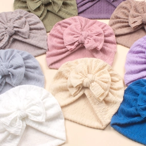 Flat lay of colorful knitted baby turban hats with large bows in nine vibrant shades