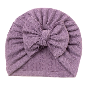 Close-up of baby purple knit turban hat featuring large bow and textured cable stitch