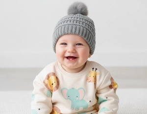 Close-up of a baby wearing a grey knitted beanie with fur pompom and a cartoon sweater