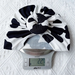 Detail shot of a lightweight cow print baby turban hat weighing only 22.7g on a scale
