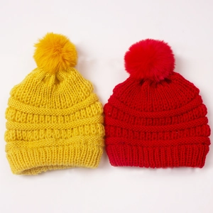 Winter knitted baby hats in yellow and red with large fluffy pom poms and thick ribbed texture