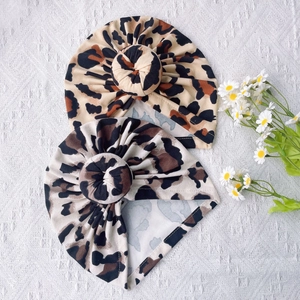 Flat lay of leopard print donut knot turban hats for infants on a woven texture mat