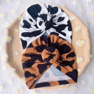 Detailed set of two baby donut hats featuring black and brown cow patterns on soft cotton