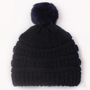 Detail of navy blue cable knit baby hat featuring a large soft faux fur pom-pom topper