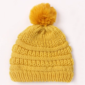 Close-up detail of mustard yellow knit baby hat with soft pom-pom and thick texture