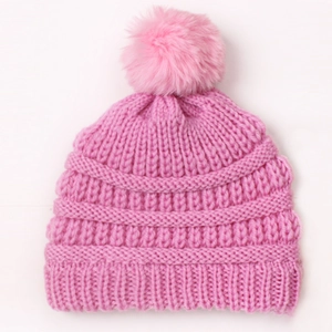 Detailed view of pink knitted baby hat with fluffy faux fur pompom and soft texture