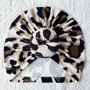 Detail view of baby leopard print turban hat with a cute top knot on a soft knit background