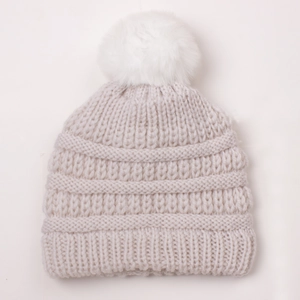 Close-up of baby winter knit hat with chunky knit texture and white faux fur pompom