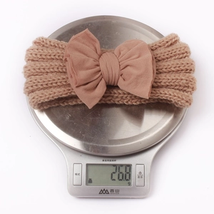 Gewichtsdetail eines 26,8g braunen Strick-Stirnbands für Babys mit großer Schleife auf Waage
