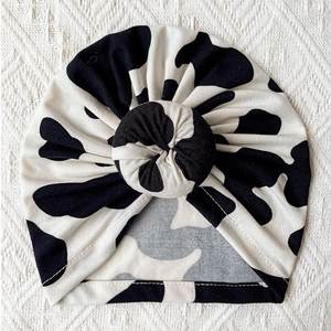 Detail of baby turban hat featuring black and white cow print and knotted top design