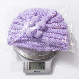 Detail der lila Baby-Strickmütze mit Blume auf einer Waage mit Gewicht 45,5g