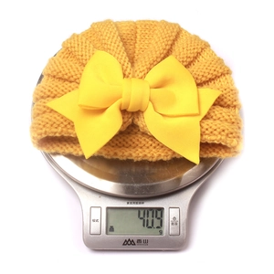 Détail d'un bonnet bébé en maille jaune avec grand nœud pesant 40,9g sur une balance