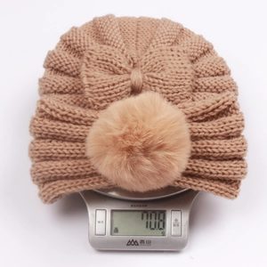 Detailed close-up of a warm khaki knitted baby beanie with faux fur pom and bow detail