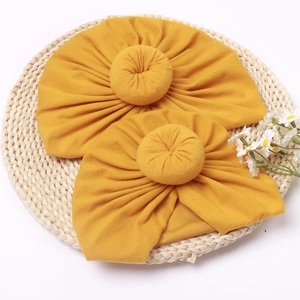 Détail de bonnets turban bébé jaune vif avec nœud donut sur un fond de tapis tissé
