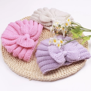 2-piece baby knitted turban hats with large bows in pink, beige, and purple on a mat